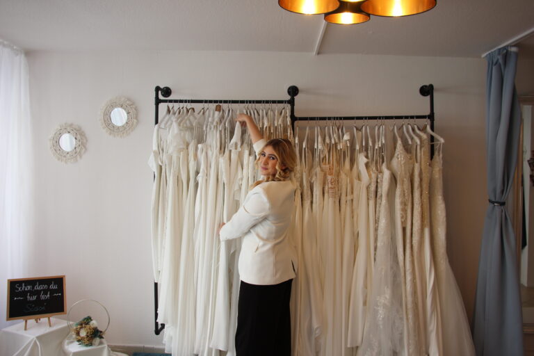 Besitzerin Caro hängt in ihrem Atelier "la vie en rose" ein Brautkleid zwischen andere Brautkleider auf eine Kleiderstange.