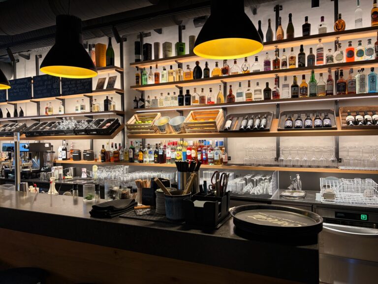 Professionelle Bar im Anders mit beleuchteten Regalen, gefüllt mit Spirituosen, Weinen und Gläsern.