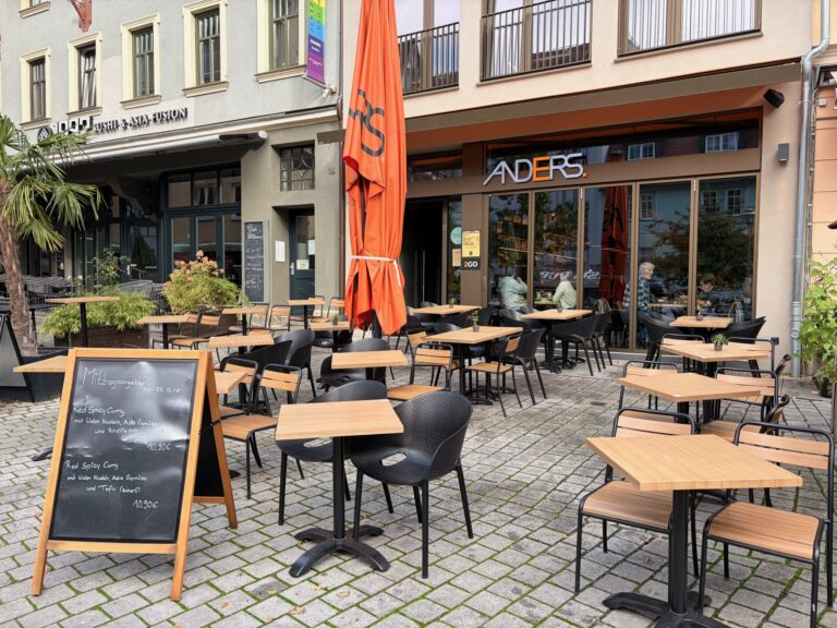 Außenansicht des Café Anders Jena mit großer, orangefarbener Markise, Außenterrasse und Tafel mit Mittagsangebot.