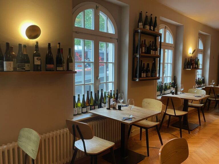 Gemütliche Fensternische mit Tischen, die Fensterbänke und Regale sind gesäumt mit zahlreichen Weinflaschen.