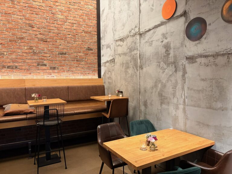 Innenraum des Café Anders mit Bank aus braunem Leder, Holztischen und einer dekorativen Ziegelwand.