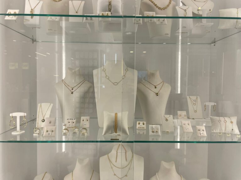 Nahaufnahme einer Glasvitrine, in der goldene Halsketten, Ohrringe und Armbänder auf weißen Büsten und Ständern präsentiert werden.