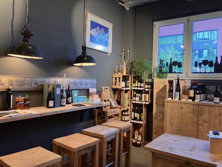 Innenraum der Vinothek mit dunklen Wänden, rustikalen Holzregalen, Industrielampen und einem zentralen Verkostungstisch.