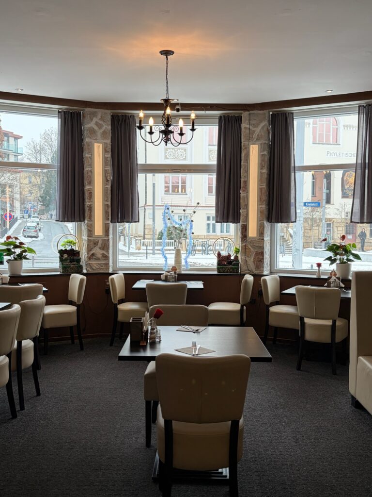 Tische und Stühle stehen vor großen Fenstern in einem Restaurant