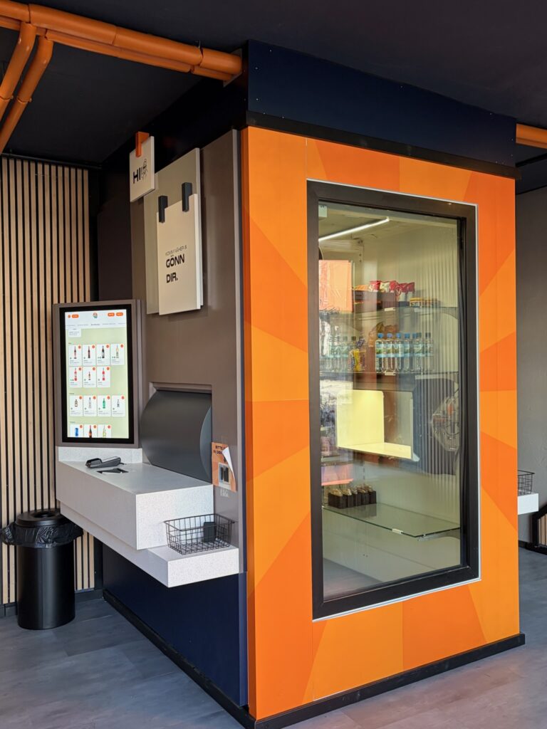 Innenansicht des Verkaufsbereichs von Tante Zukunft mit dem Ausgabeschacht, Terminal und knallig orangefarbenem Design.