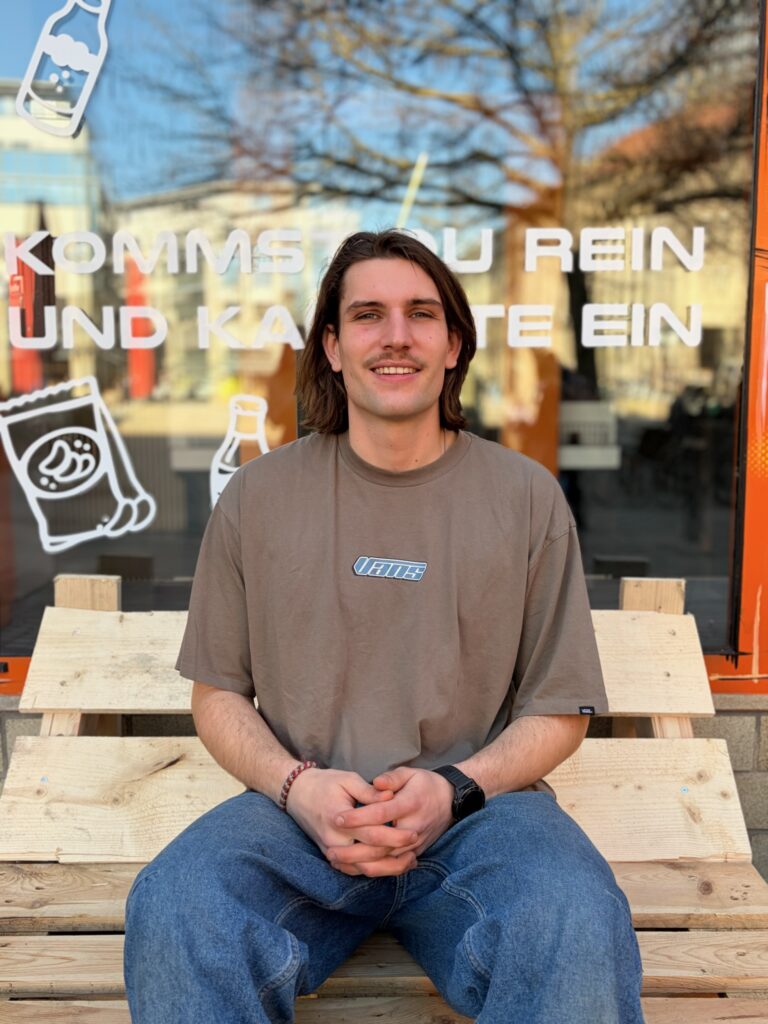 Porträt von Willy, einem der Gründer von Tante Zukunft, sitzend vor der Fensterfront seines Ladens in Jena.