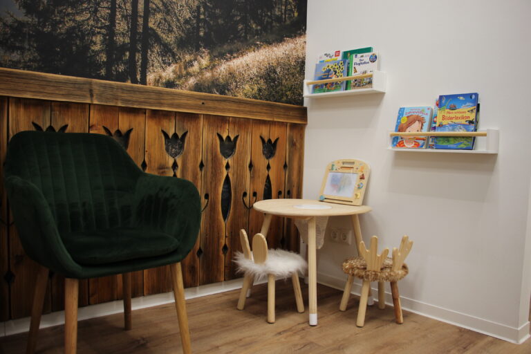 Kinderspielecke in der Zähnerie mit kleinem Tisch, Bücherregal und tierförmigen Stühlen.