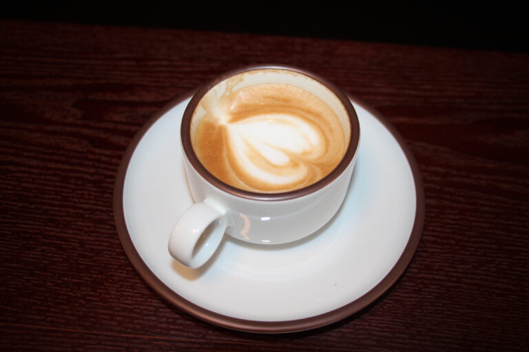 Eine Tasse Cappuccino mit detailreicher Herz-Latte-Art auf einem weißen Unterteller.