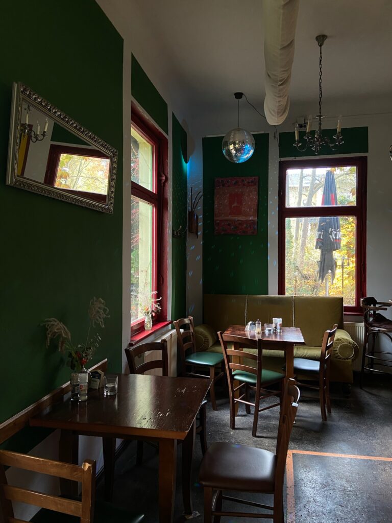 Sitzbereich mit grünen Wänden, roten Fensterrahmen und einer Discokugel an der Decke; Sonnenlicht fällt herein.