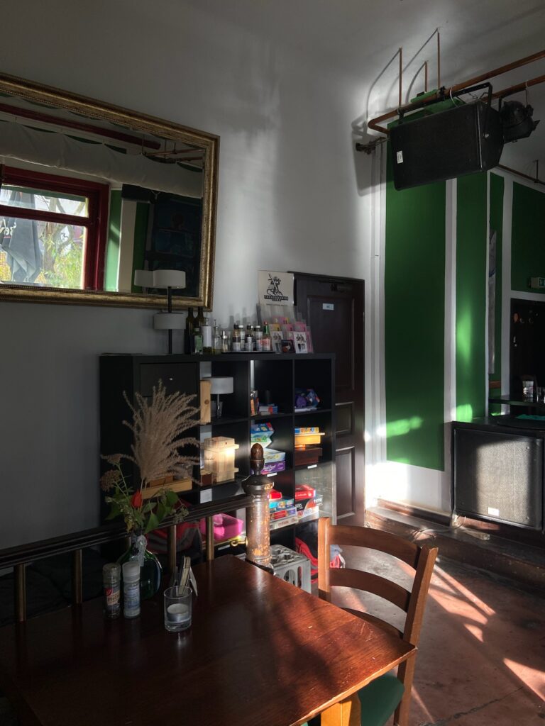 Gemütliche Ecke mit dunklem Holztisch, Goldrahmen-Spiegel und einem Regal voller Gesellschaftsspiele.