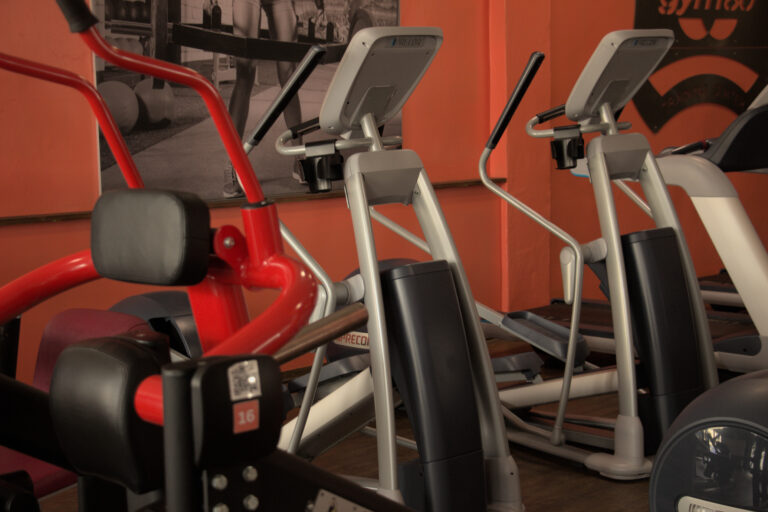 Reihe von modernen Precor Crosstrainern im Cardio-Bereich des Bodyfit Studios vor einer orangen Wand.