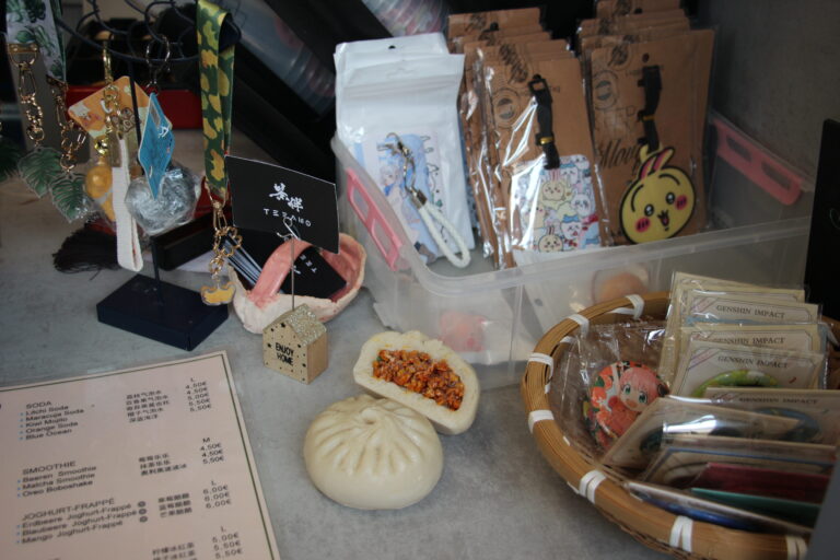 Tischansicht mit aufgeschnittenem, gefülltem Baozi, ganzem Baozi, Speisekarte und Merchandise-Artikeln.