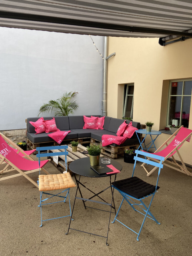 Gemütliche Außenlounge im Innenhof des Aquamarin mit Palettenmöbeln, pinken Kissen und Liegestühlen.