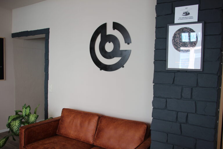 Moderner Wartebereich mit braunem Ledersofa, Pflanze und Wanddeko mit dem Logo der Fahrschule Cartel.