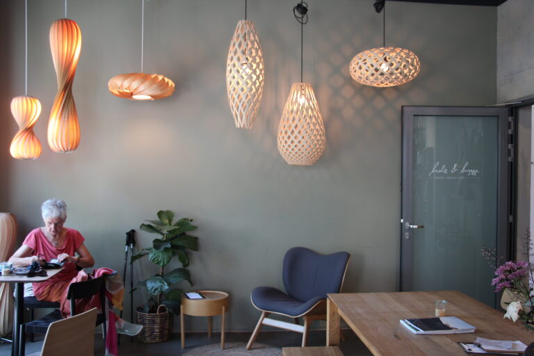 Innenraum des Cafés mit grauen Wänden, skandinavischen Designmöbeln und auffälligen, geschwungenen Holz-Pendelleuchten.