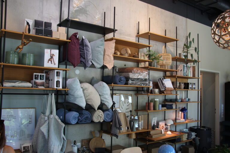 Regalwand im Industrial-Stil vor einer Betonwand, gefüllt mit bunten Kissen, Decken und Wohnaccessoires.