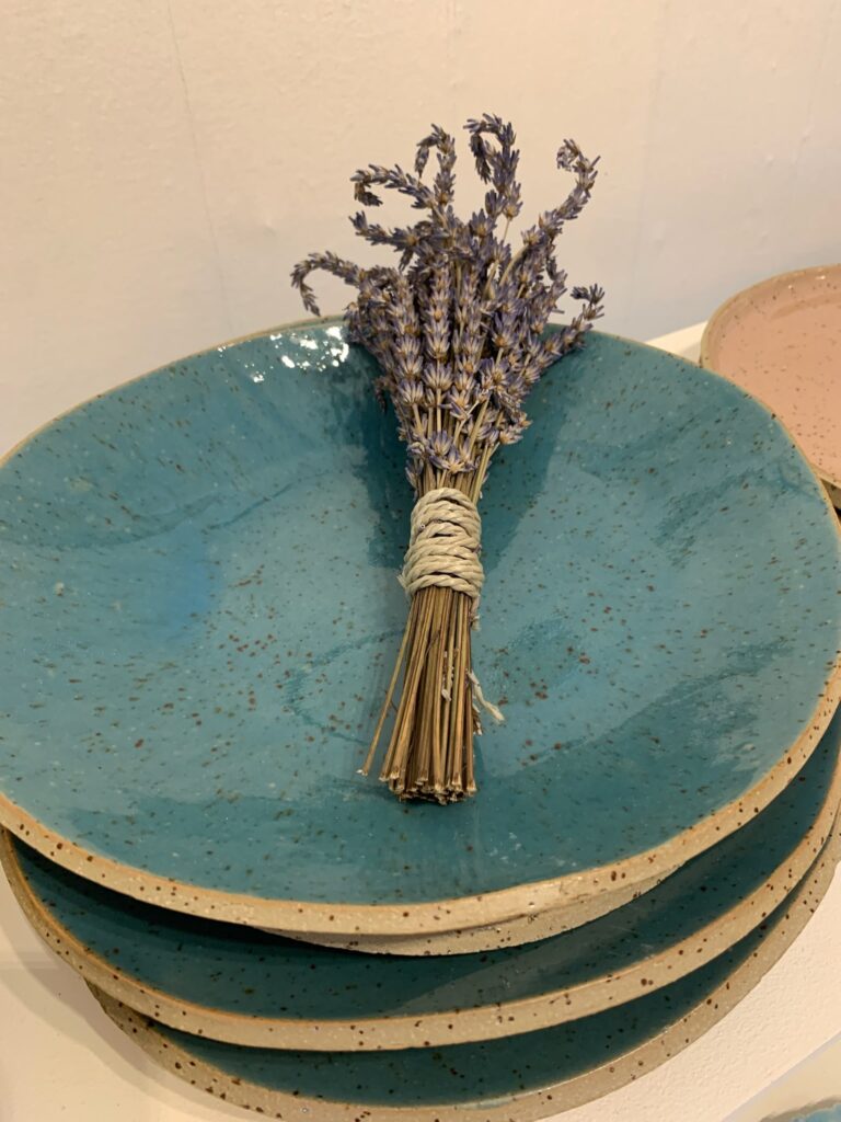 Stapel handgetöpferter Keramikteller in Beige und Türkis mit Sprenkeln, darauf ein Bund getrockneter Lavendel.