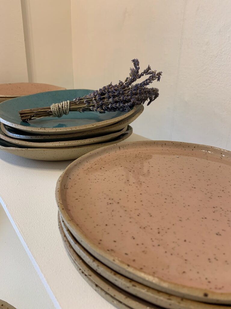 Draufsicht auf leuchtend türkisfarbene Keramikteller mit braunen Sprenkeln und einem Lavendelstrauß in der Mitte.