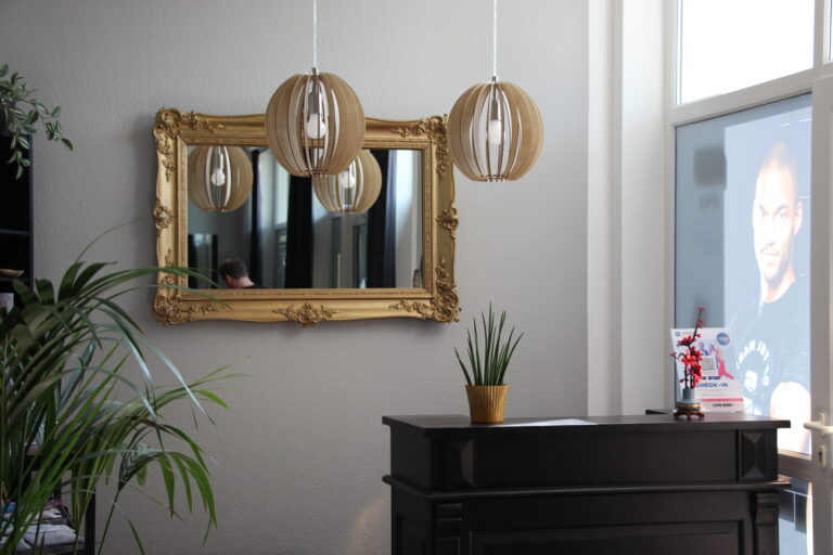 Stilvoller Eingangsbereich mit dunklem Holztresen, goldenem Barockspiegel an der Wand und modernen Lamellen-Pendelleuchten.