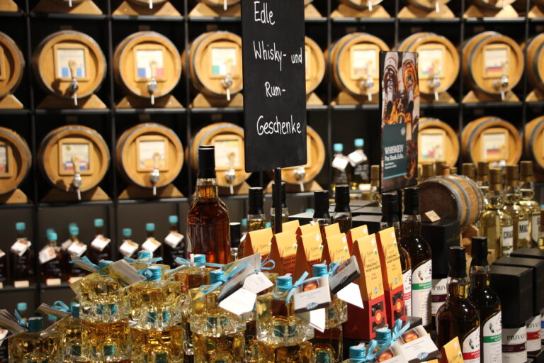 Präsentationstisch mit verschiedenen Geschenkflaschen, darunter stapelbare Flaschensysteme, und einem Schild "Edle Whisky- und Rum-Geschenke".