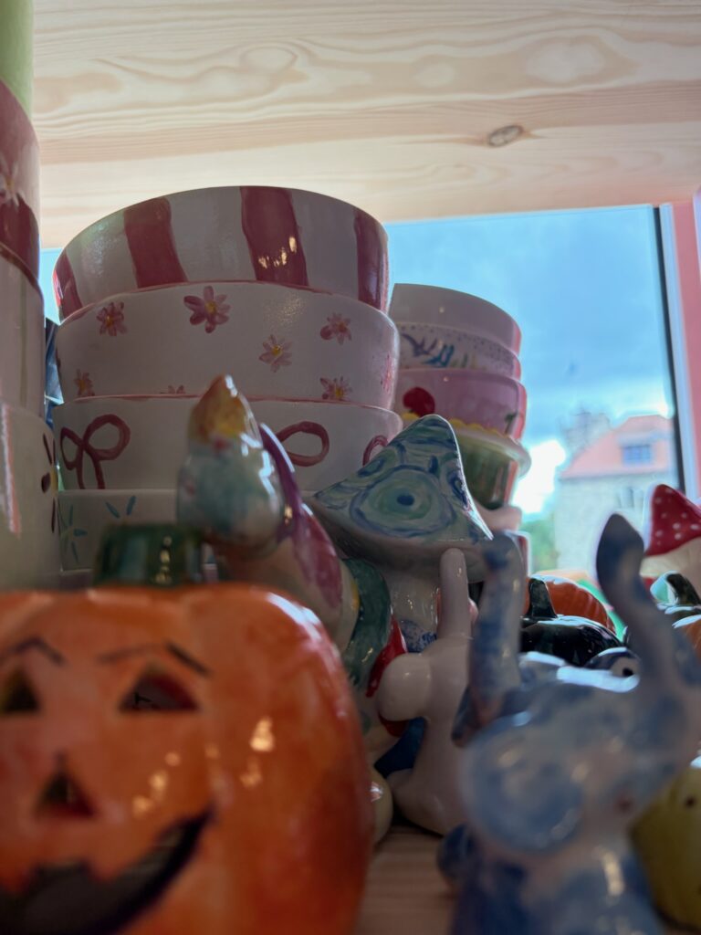 Bemalte Keramikfiguren und Schalen in einem Atelier oder Geschäft, bunt gestaltet und ausgestellt auf einem Regal.