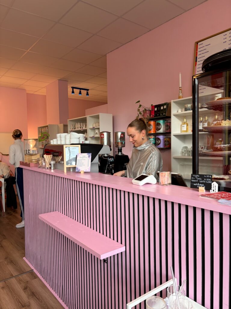Innenaufnahme von Poppy’s in Jena mit pinker Theke, selbstgebauter Einrichtung und Barista beim Zubereiten von Kaffee.