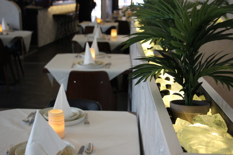 Eleganter Innenraum des Naan n Curry mit weiß gedeckten Tischen, Kerzenlicht und einer beleuchteten Pflanzen-Deko.