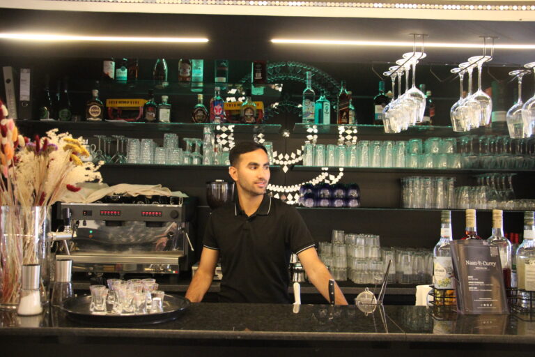 Bartender im Naan n Curry hinter der schwarzen, beleuchteten Bar.