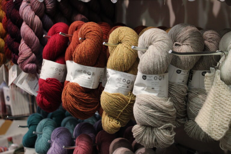 Hängende Stränge dicker, hochwertiger Garne in Rot, Ocker und Grau mit deutlich sichtbaren Garnetiketten.