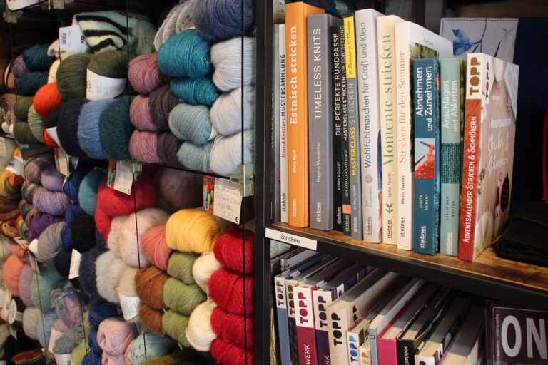 Regal mit Fachliteratur zum Stricken und Häkeln neben Wollregalen in Fadenwohl.
