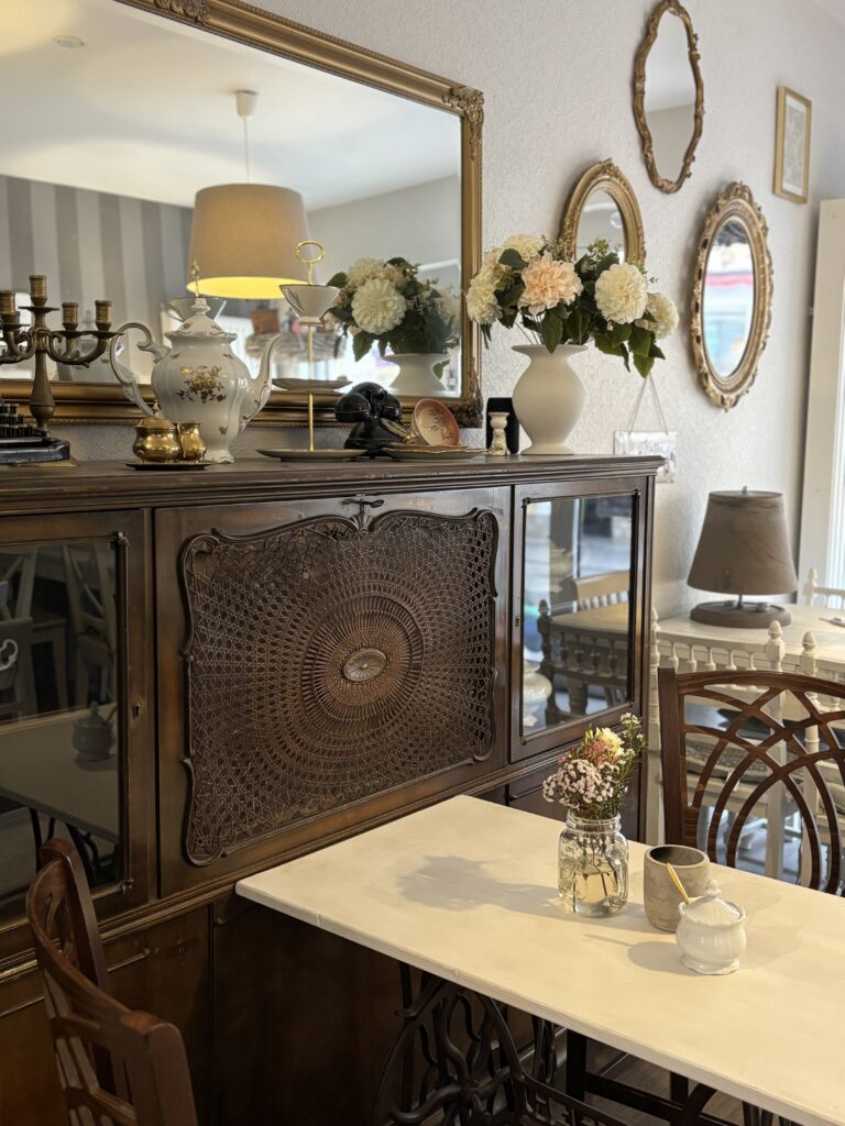 Antikes dunkles Holzbuffet mit weißem Porzellan, Spiegeln und Blumenarrangements im Lotti's Café Jena.