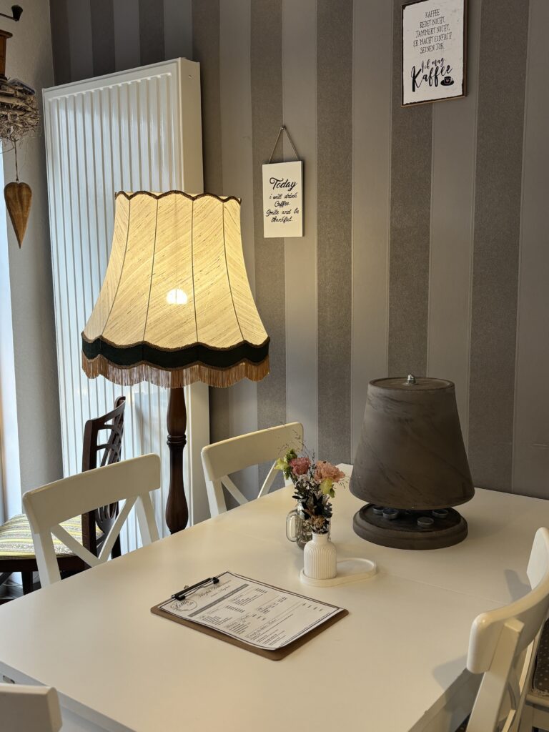 Gemütliche Sitzecke mit weißem Tisch, Stühlen und einer großen Vintage-Stehlampe mit Fransen im Lotti's Café Jena.
