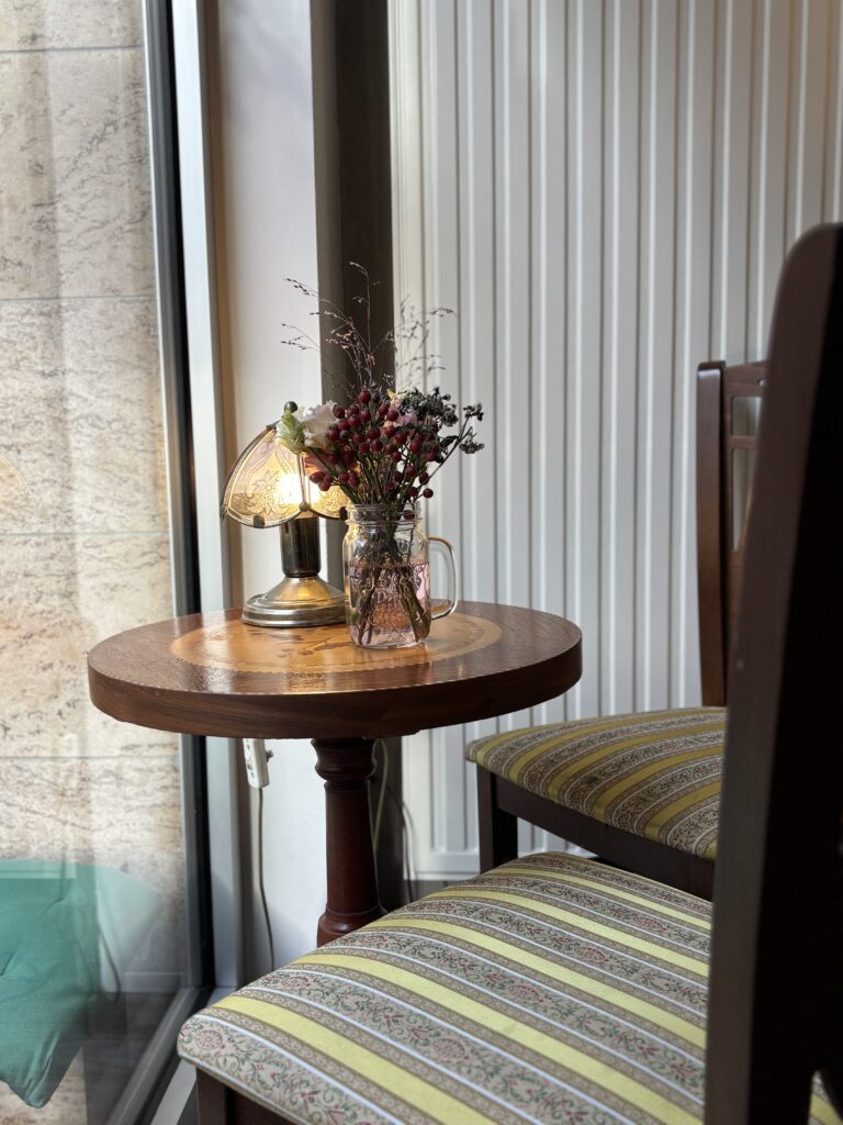 Kleiner runder Holztisch am Fenster mit antiker Lampe und Blumenstrauß im Lotti's Café.