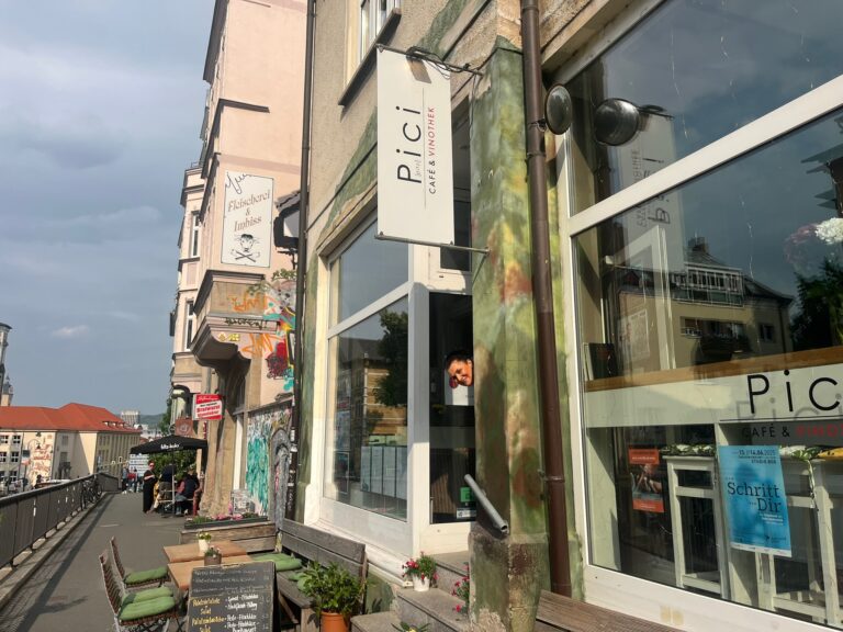 Außenfassade des Pici Café & Vinothek in Jena, eine Mitarbeiterin schaut spielerisch und einladend zur Tür heraus.