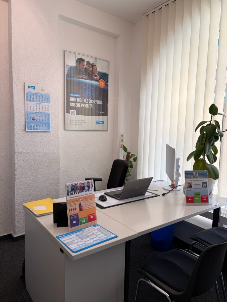 Heller Schreibtisch für Kundenberatung mit Laptop, Besucher-Stühlen, einer Pflanze und einem Poster zum Thema digitale Sicherheit.