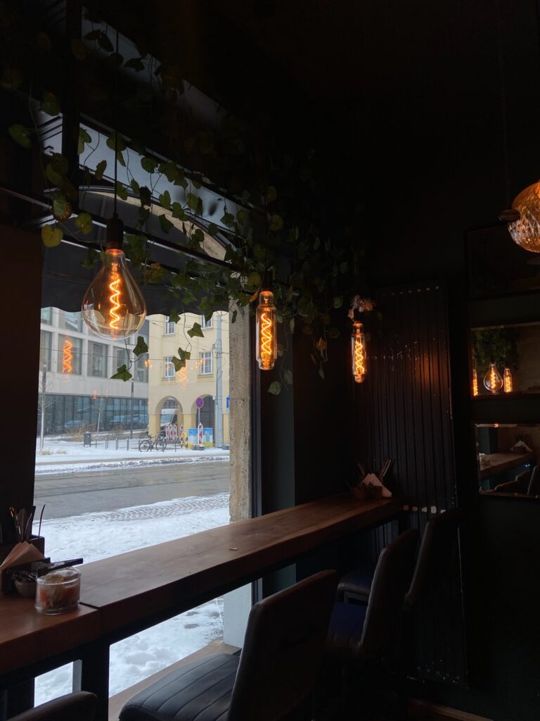 Hohe Barhocker an einem langen Holztisch direkt am großen Fenster mit Blick auf eine verschneite Straße in Jena.