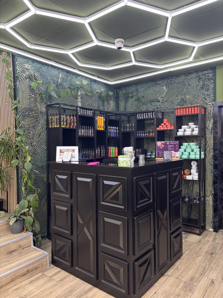 Schwarzer Empfangstresen in einem Barbershop mit Regalen voller Haarpflegeprodukte unter einer modernen Wabenbeleuchtung.