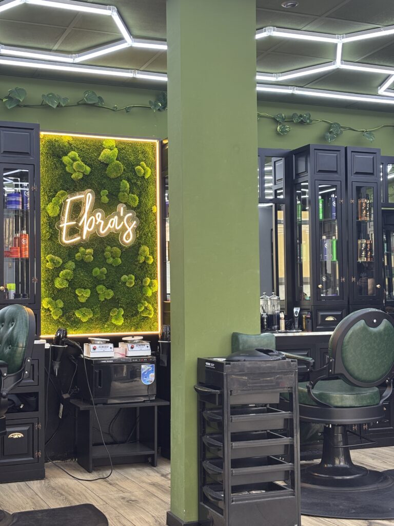 Eine beleuchtete grüne Mooswand mit dem leuchtenden Schriftzug "Ebra's" zwischen zwei schwarzen Regalschränken.