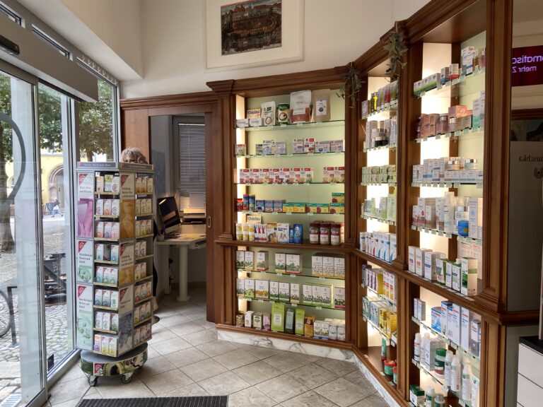 Blick in den hellen Verkaufsraum mit einem Regal voller Tees und Naturheilmittel; durch die große Glastür sieht man das Kopfsteinpflaster des historischen Marktplatzes.