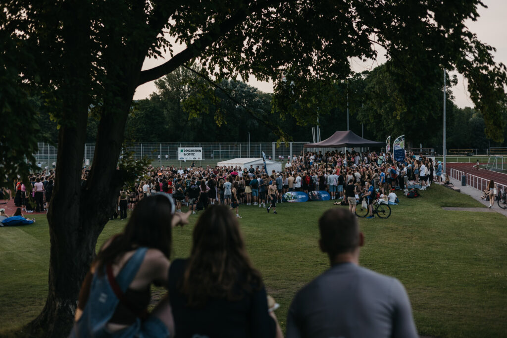 Große Menschenmenge versammelt sich in der Abenddämmerung auf einer Wiese vor einer Bühne beim Summer Dance Event.