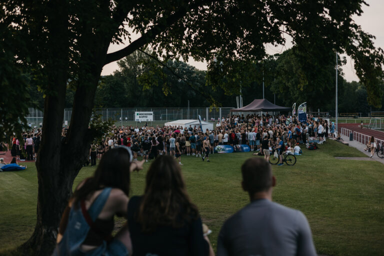 Große Menschenmenge versammelt sich in der Abenddämmerung auf einer Wiese vor einer Bühne beim Summer Dance Event.