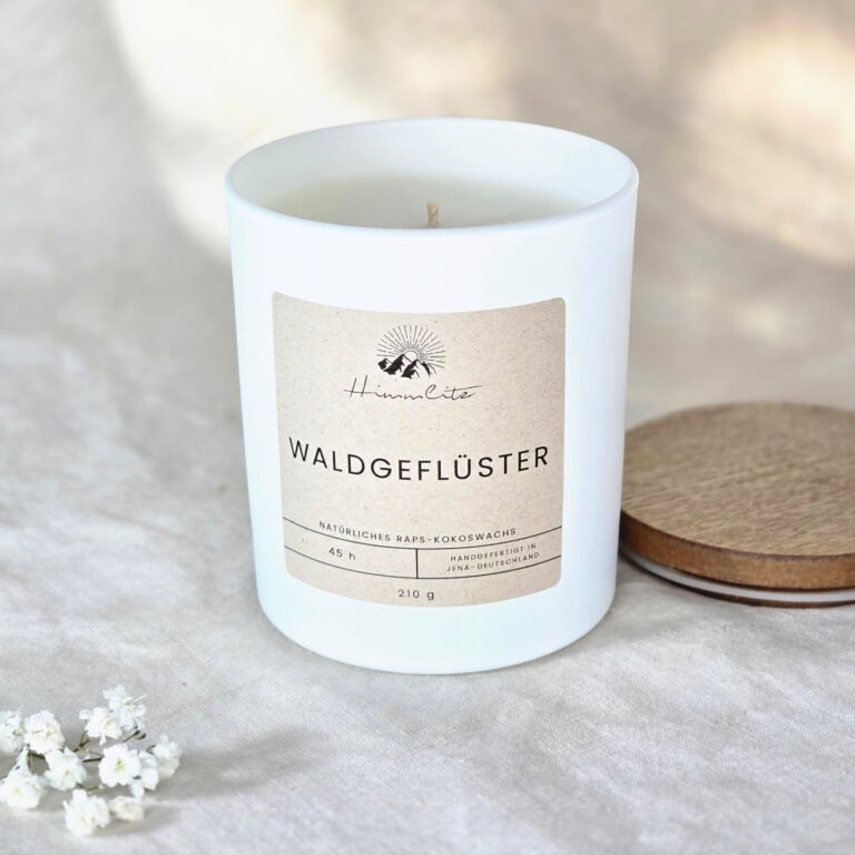 Weiße Duftkerze mit dem Label „Waldgeflüster“ steht auf einen weißen Stoff neben einem Holzdeckel