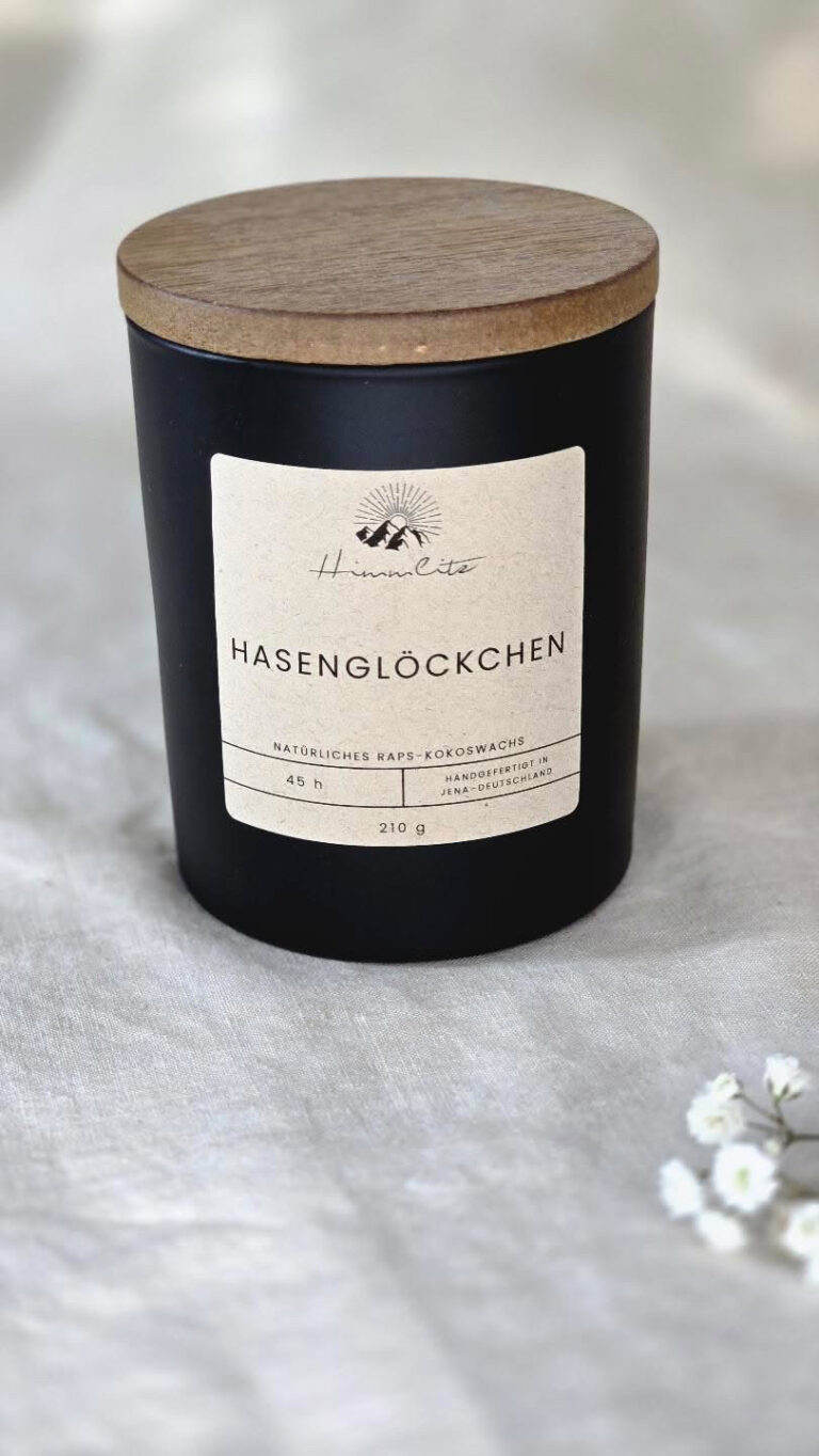 Schwarze Duftkerze mit Holzdeckel und Aufschrift „Waldgeflüster“ steht auf hellem Untergrund