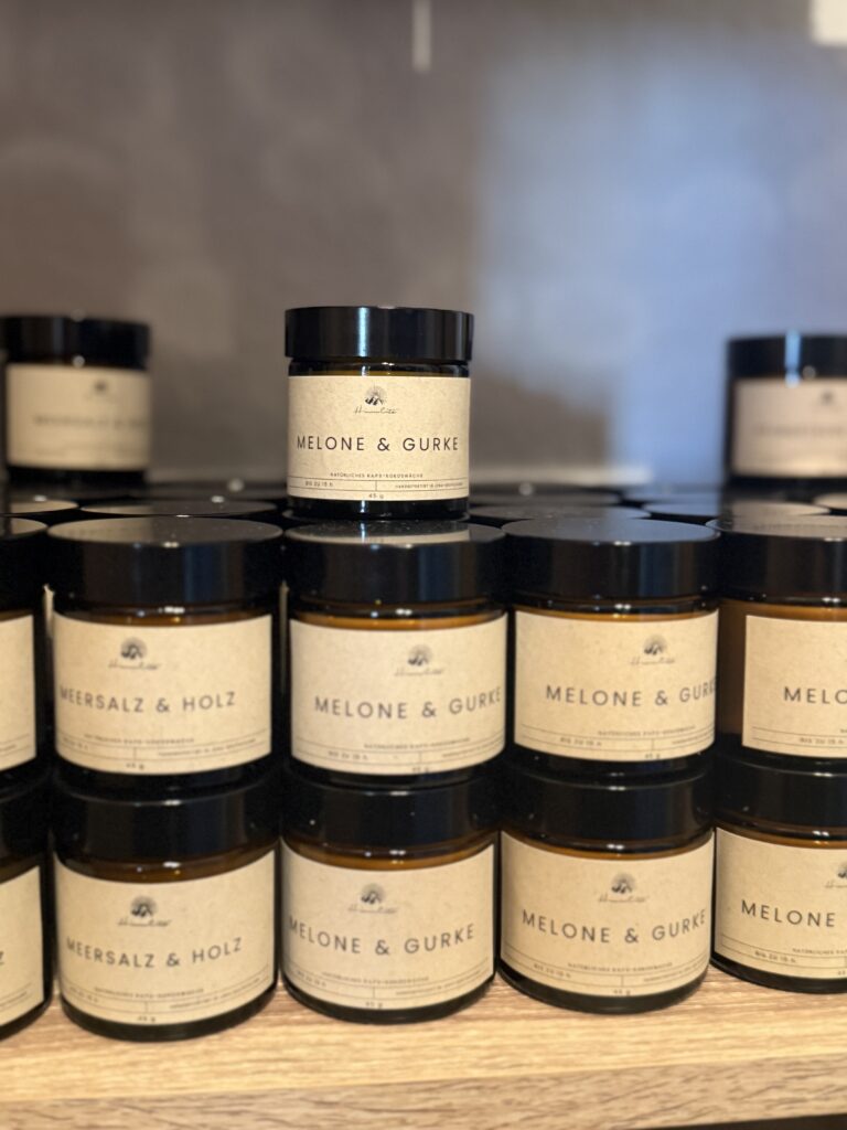 Mehrere kleine Duftkerzen in braunen Gläsern stehen gestapelt auf einem Regal