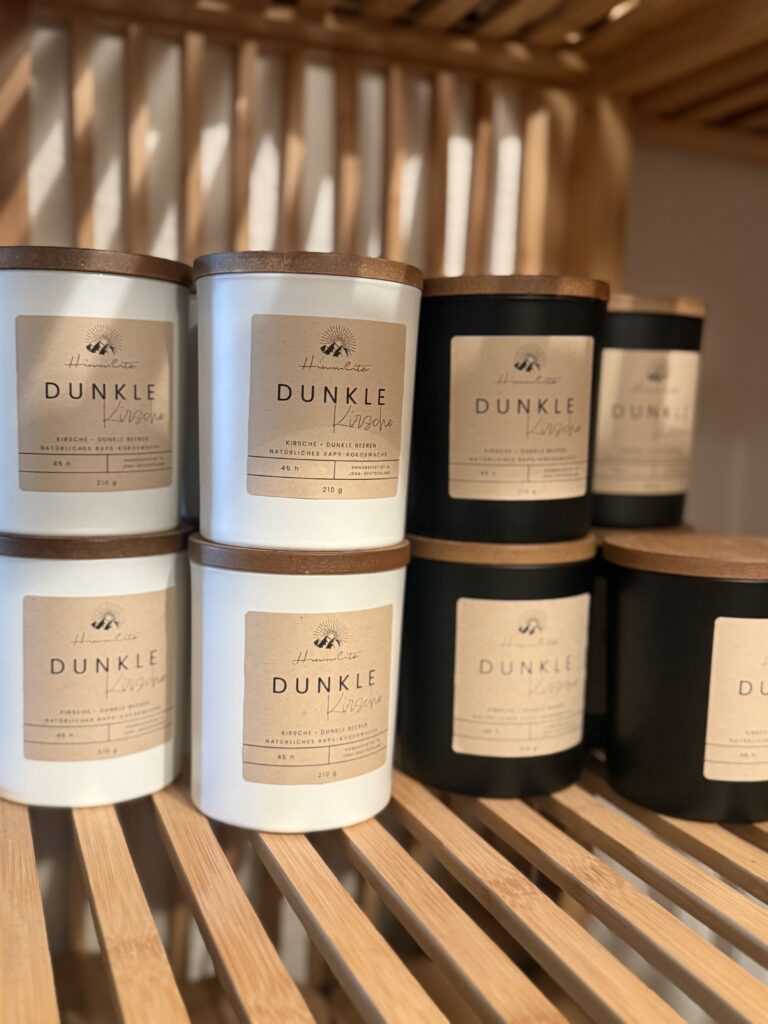Mehrere große Duftkerzen mit der Aufschrift „Dunkle Kirsche“ stehen in einem Holzregal