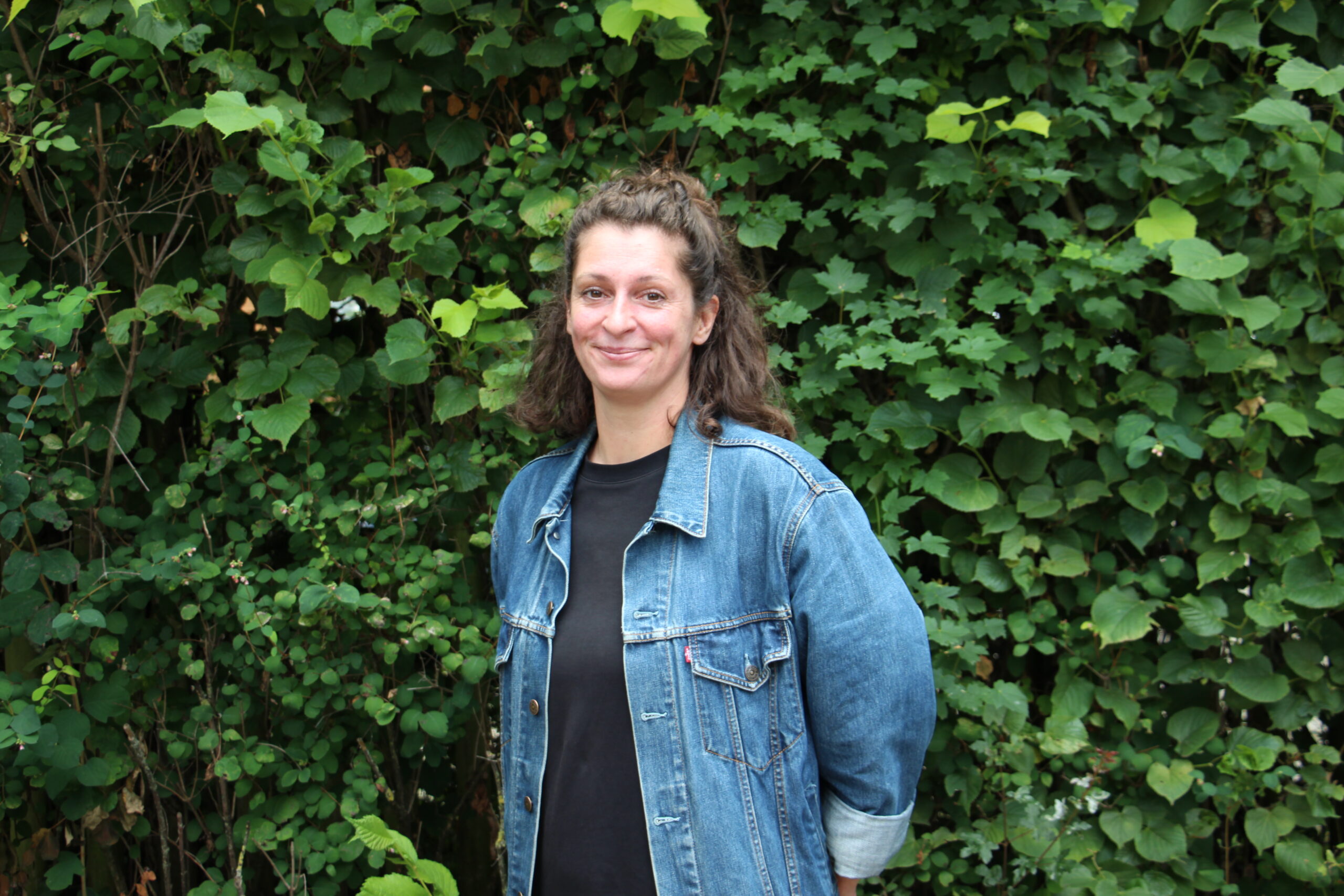 Citymanagerin Katja Eisenschmidt der Initiative Innenstadt Jena e.V. steht lächelnd vor einer grünen Hecke in Jena.