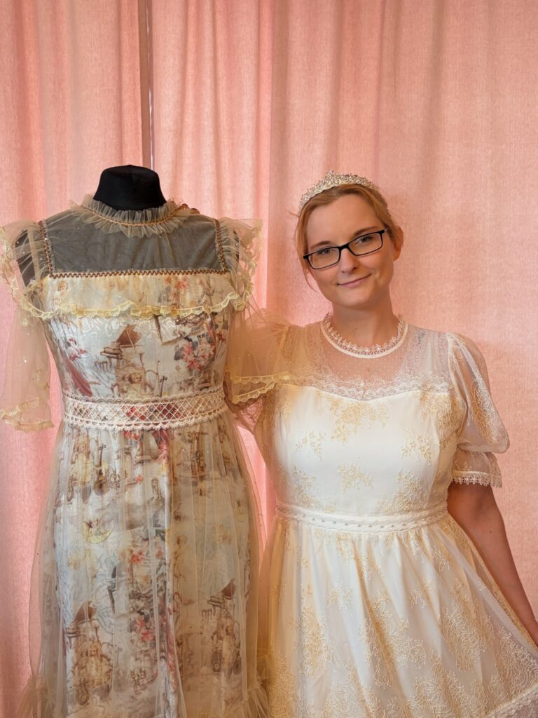 Modedesignerin Jan lächelt neben einer Schneiderpuppe mit einem ihrer Designs; sie trägt selbst ein weißes Lolita-Kleid und ein Diadem.