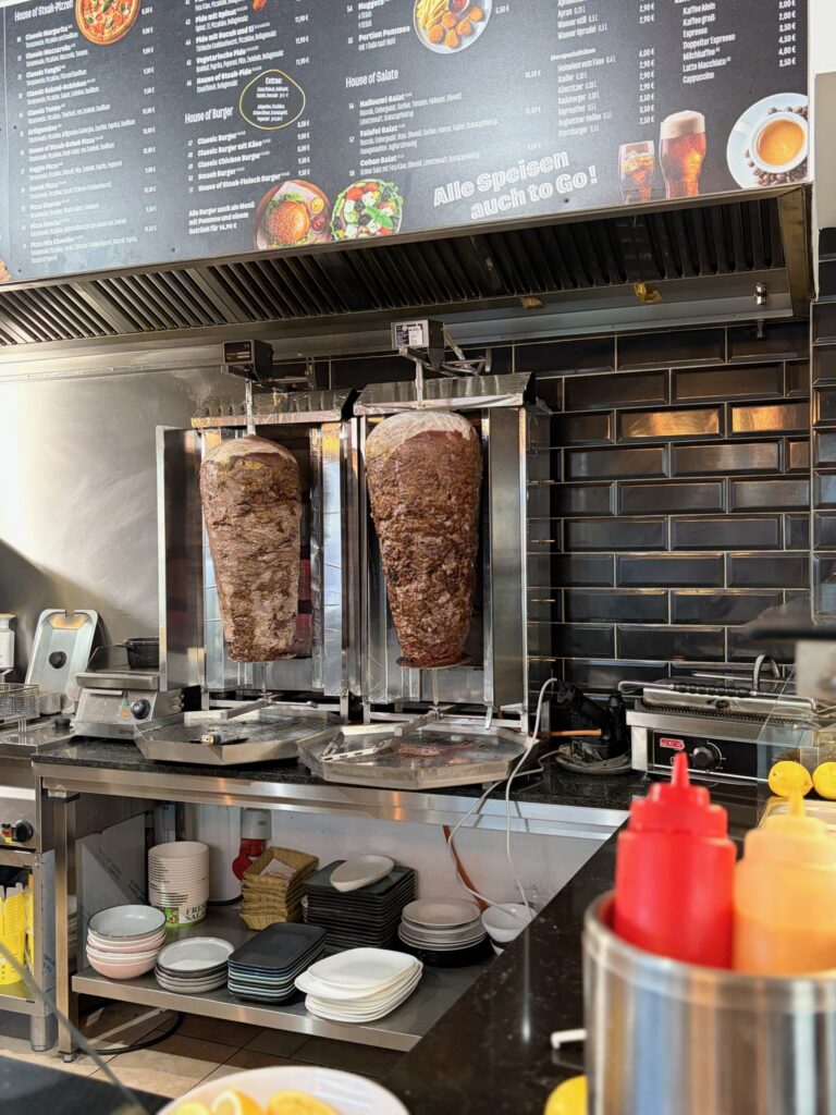 Zwei Döner-Spieße stehen in einer Küche neben Geräten und Arbeitsfläche