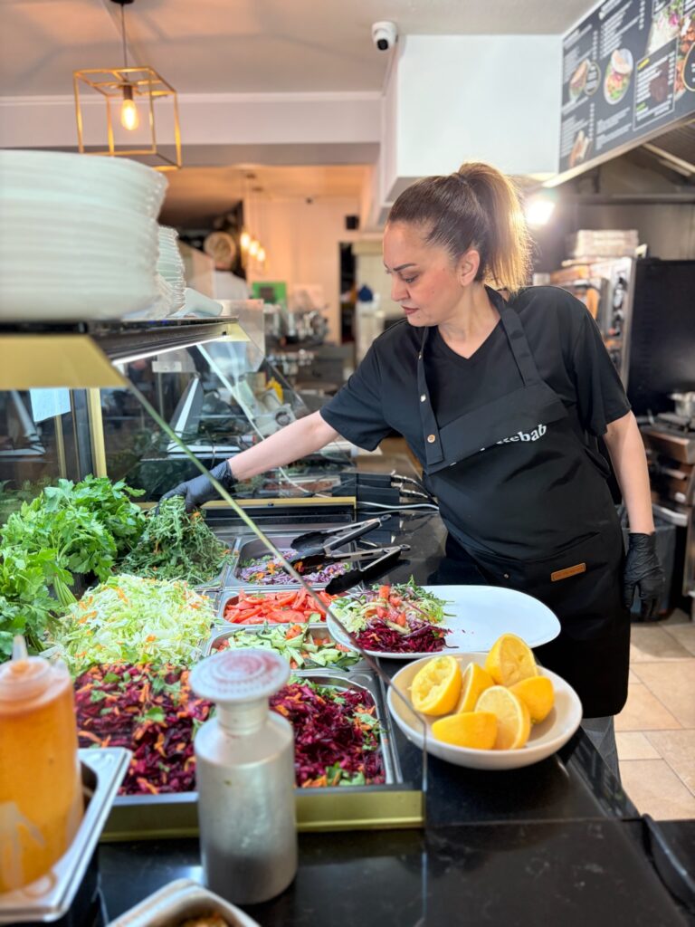 Diana steht an einer Theke und richtet einen Teller mit Salat und Zutaten an.