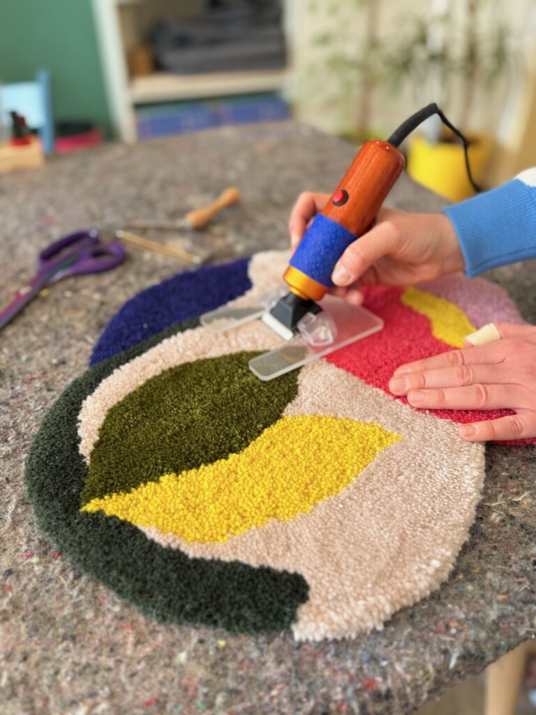 Hand hält ein Werkzeug und bearbeitet die Oberfläche eines bunten Teppichs